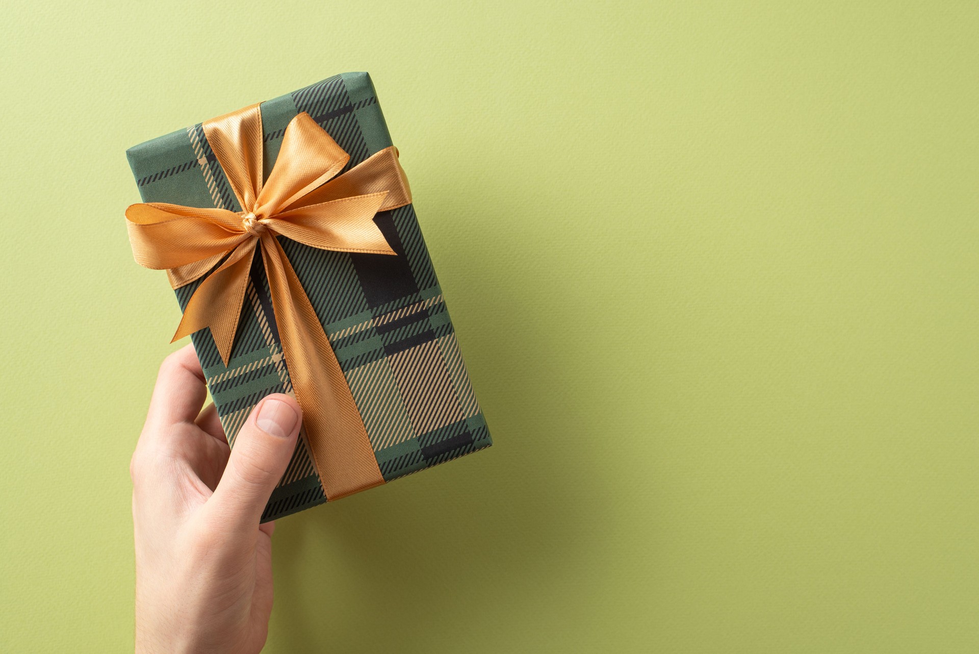 Elegante caixa de presente envolto em xadrez amarrada com uma fita dourada, guardada contra um fundo verde